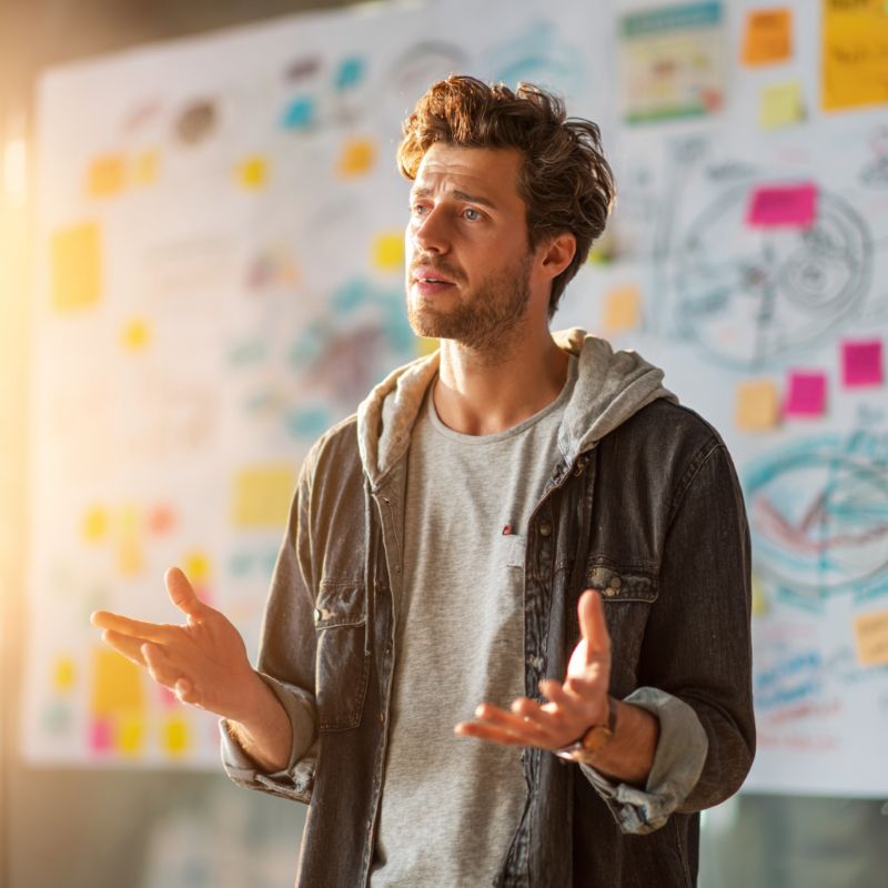 Young entrepreneur presenting a chaotic vision wall — progress over polish